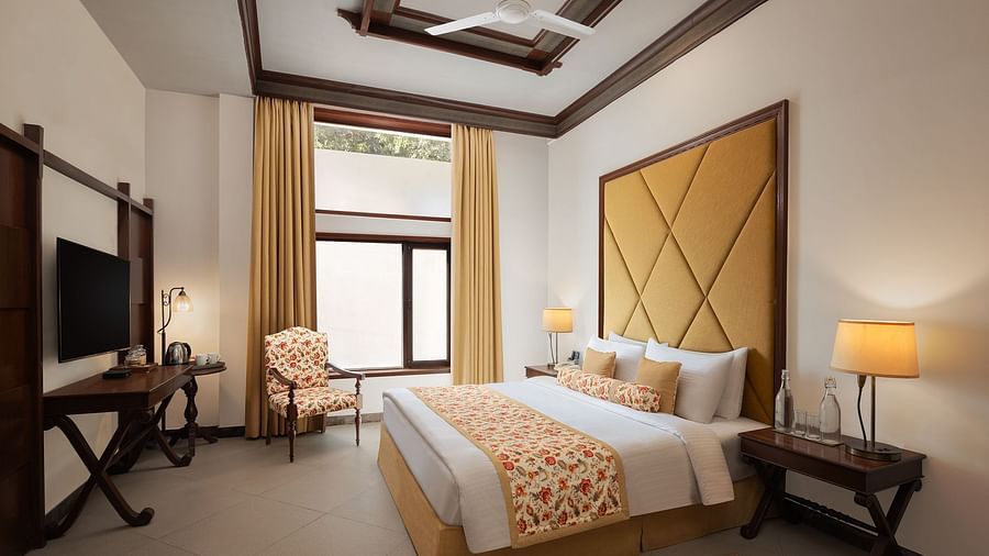 An image of a  cozy room in the naini retreat, nainital, with a double bed, wooden furniture, and a window. The room also features a ceiling fan, a TV .