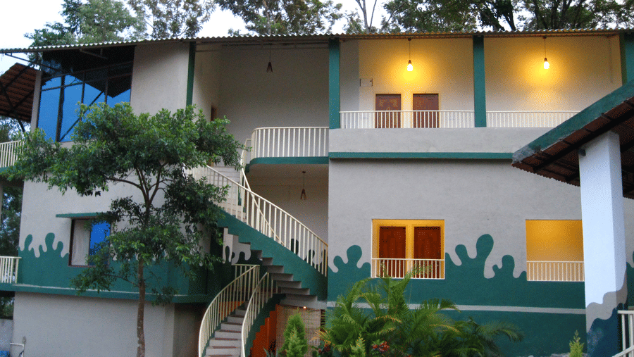 Facade of an accommodation with lights in the balcony and surrounded by plants at Coorg Jungle Camp Backwater Resort, Kushalnagar.