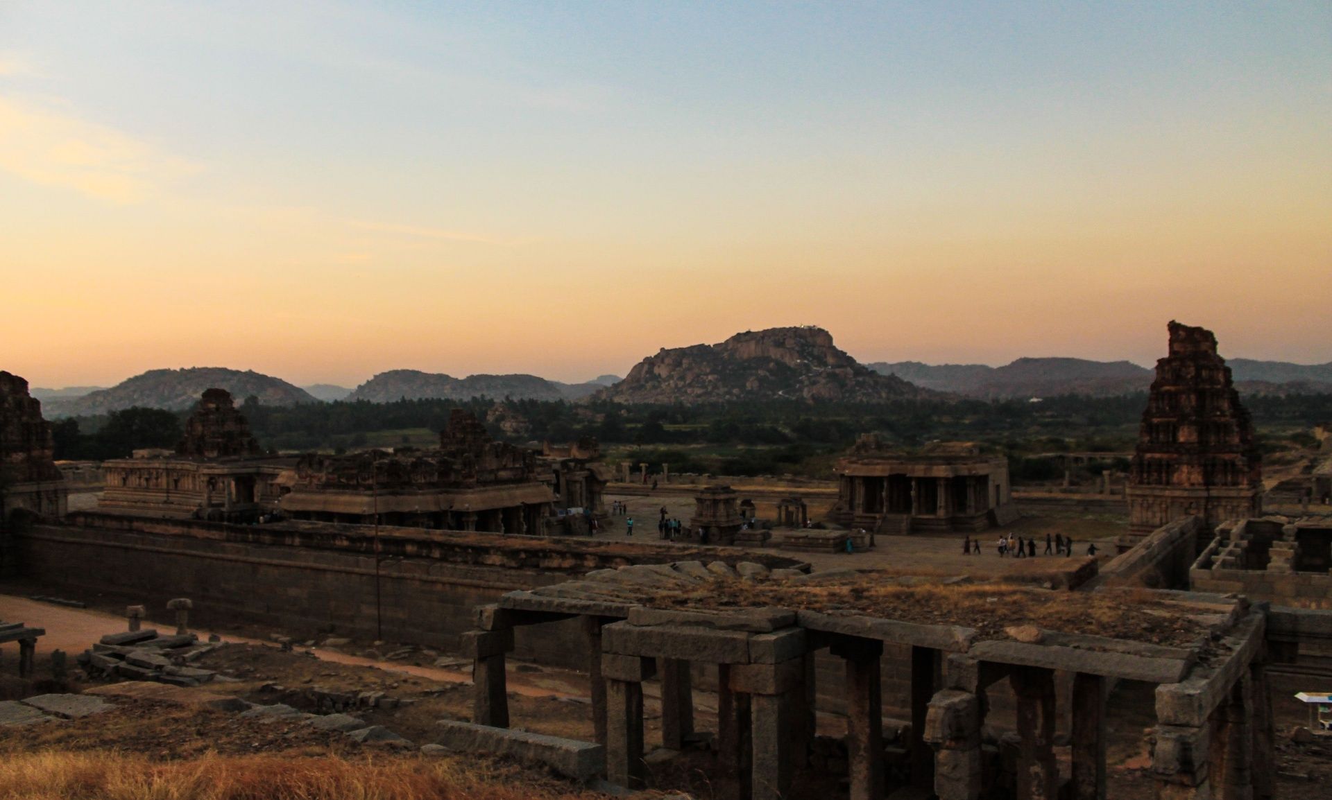 Hampi ruins at sunset with a temple complex and hills.