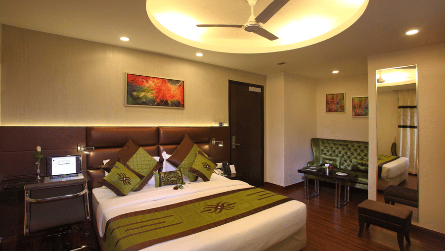 The Club Room at JRD Exortica with a double bed, wooden flooring, a ceiling fan, and modern furnishing.