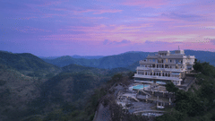Facade of Fateh Safari Suites, Kumbhalgarh featuring multiple storeys, swimming pool, lawn, sitting area, and more amidst the green hills.