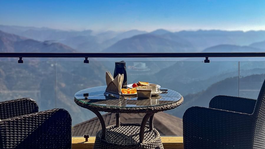 Outdoor dining setup on a balcony with panoramic Himalayan views at dusk at Aranya Himalayan Retreat, Mashobra.