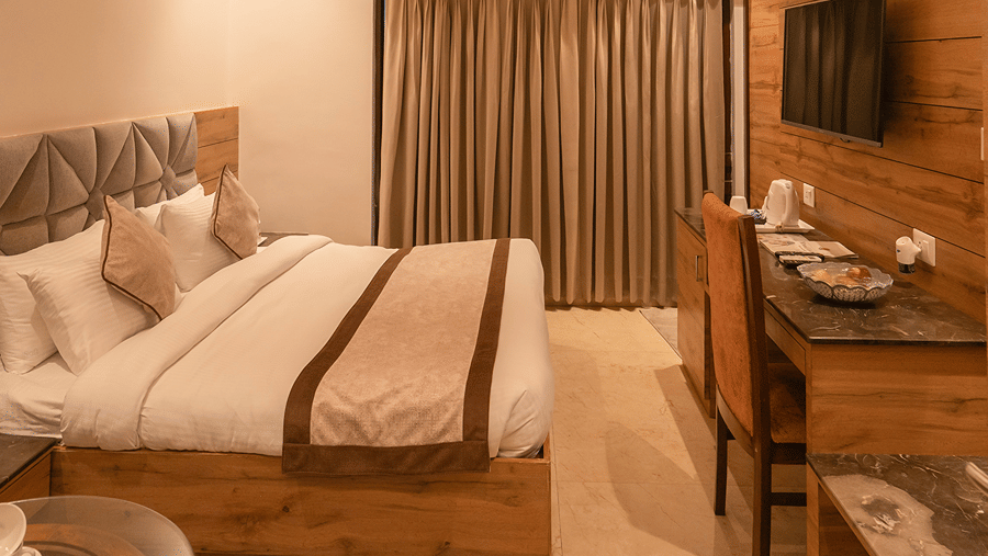 Full room view of a resort cottage featuring wooden ceilings, double bed, TV console, and study desk - Wood Castle Spa & Resort, Jim Corbett