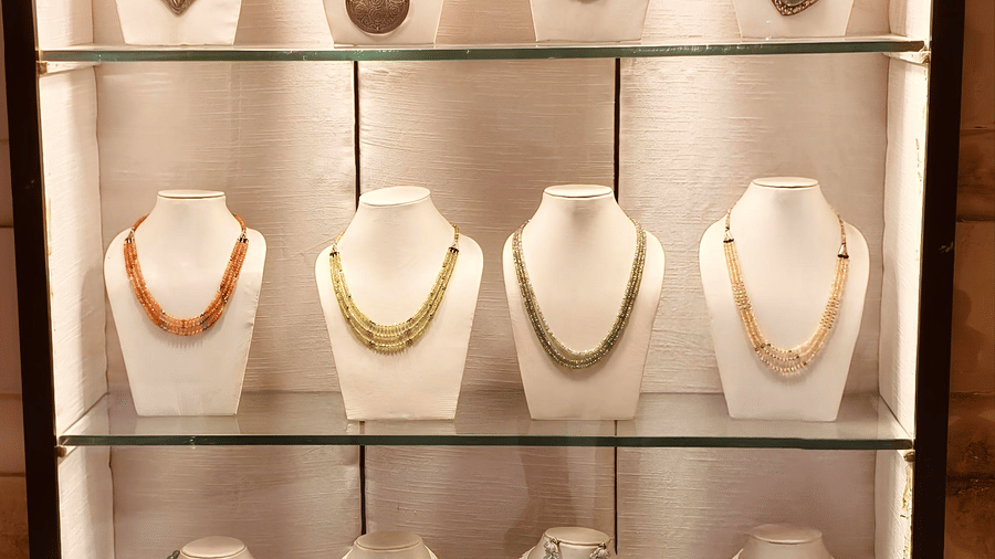 A three-tiered glass display case containing multiple necklaces on white busts | HHI Varanasi