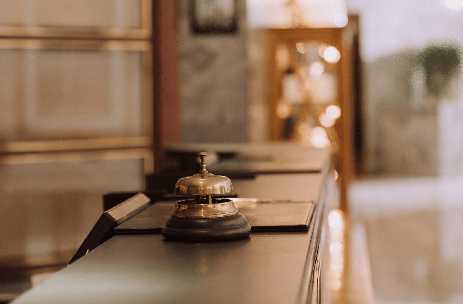 A bell kept on a wooden desk of a hotel reception lobby.