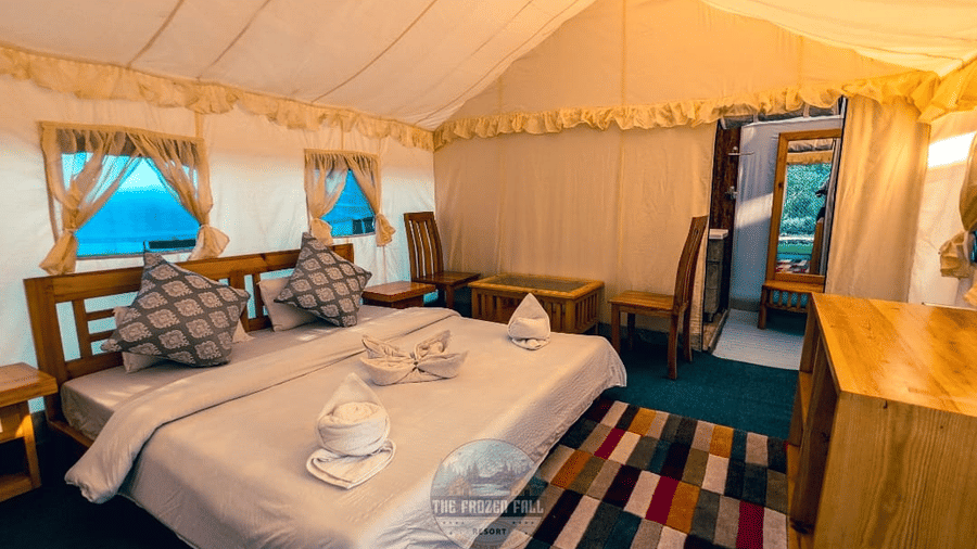 Inside a tent bedroom at Dawat e Drung by FrozenFall Resort, Drung, Tangmarg, showing a double bed, small windows, a desk and a patterned rug.