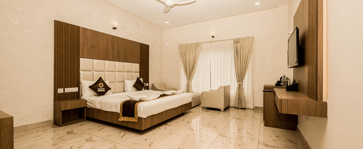 Deluxe Room With Balcony featuring a king size bed, television, and minimalist decor. - Sukhi - A Luxury Stay Inn, Chikkamagaluru