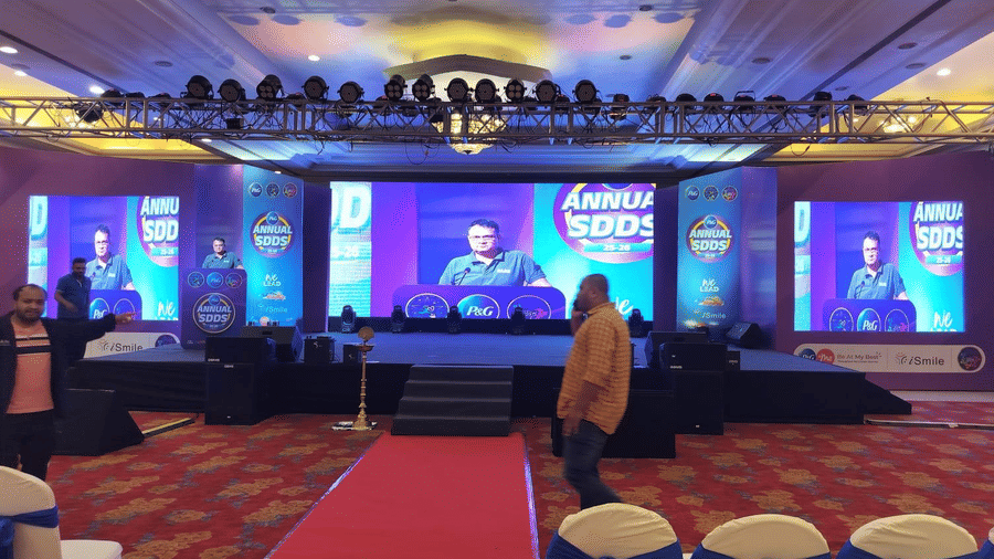 An indoor stage setup with a wide backdrop, ceiling-mounted lights, a central aisle, and seating arranged in front.