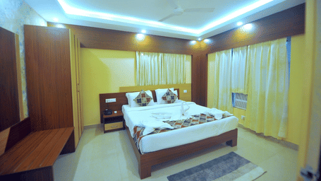 A neatly made double bed with decorative towel art inside a brightly-lit bedroom at Pipul Hotel And Resort, Puri.
