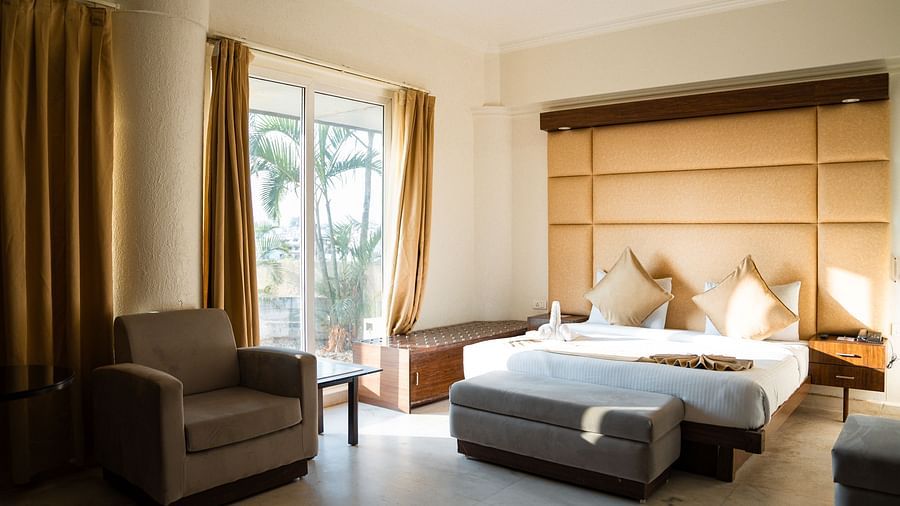 A hotel room with two separate single beds, each with yellow pillows and a padded headboard, and a sitting area with an armchair - Pride Premier Dehradun