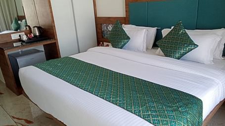 A room with a large bed which is neatly made with bedsheet, pillows and bedside tables at Angel Lords Eco Inn Amreli.