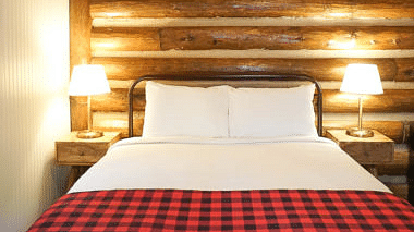 A room with a double bed and side tables with night lamps placed on it - Shaver Lake Village Hotel.