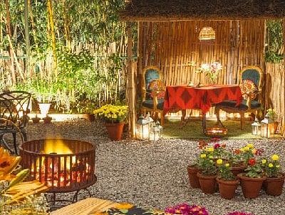 Outdoor dining setup at Karma Chalets with wooden benches, string lights, and a food counter in a garden setting.
