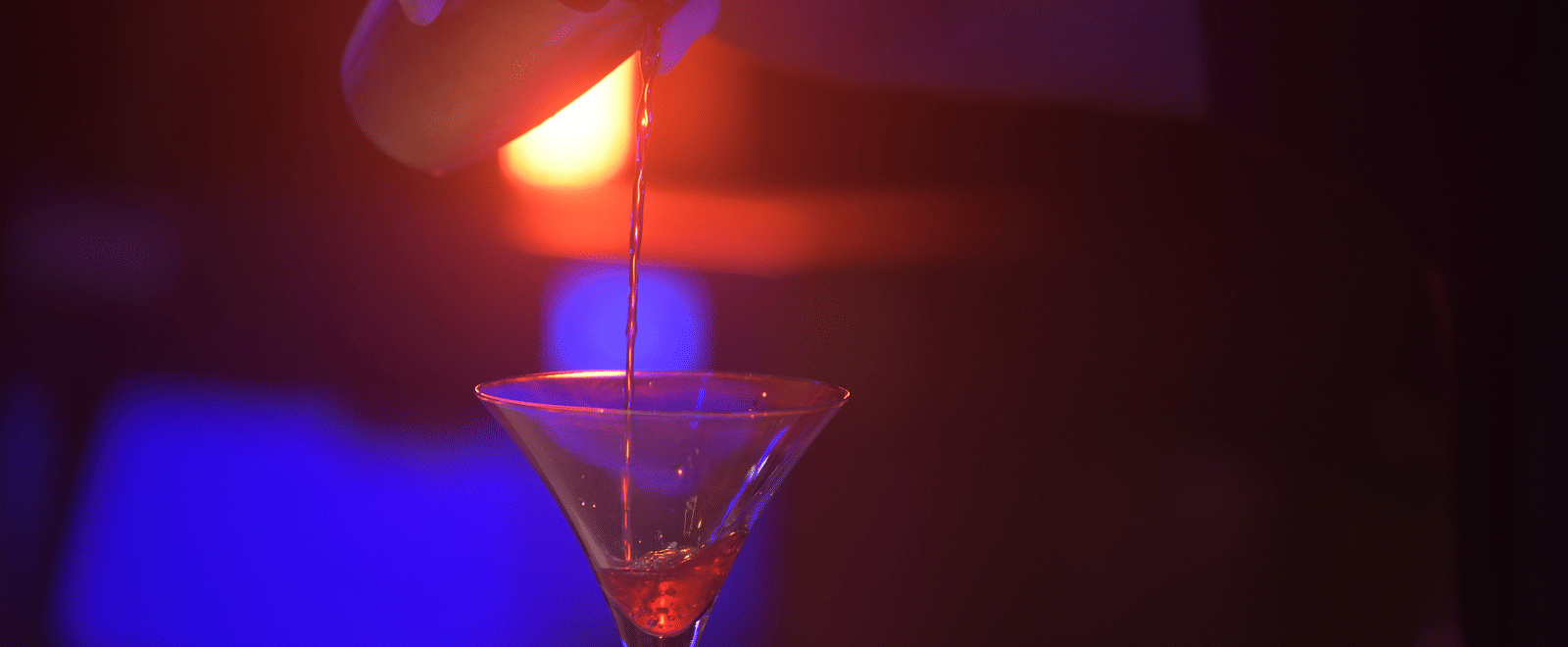 A close-up of a cocktail glass illuminated by red light, highlighting its vibrant colour at Hotel Sonar Bangla Mayapur.