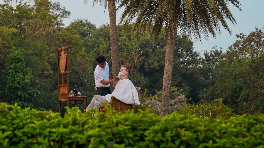 image of a man getting his beard shaved in a lawn with palm trees in the background at dev shree, deogarh