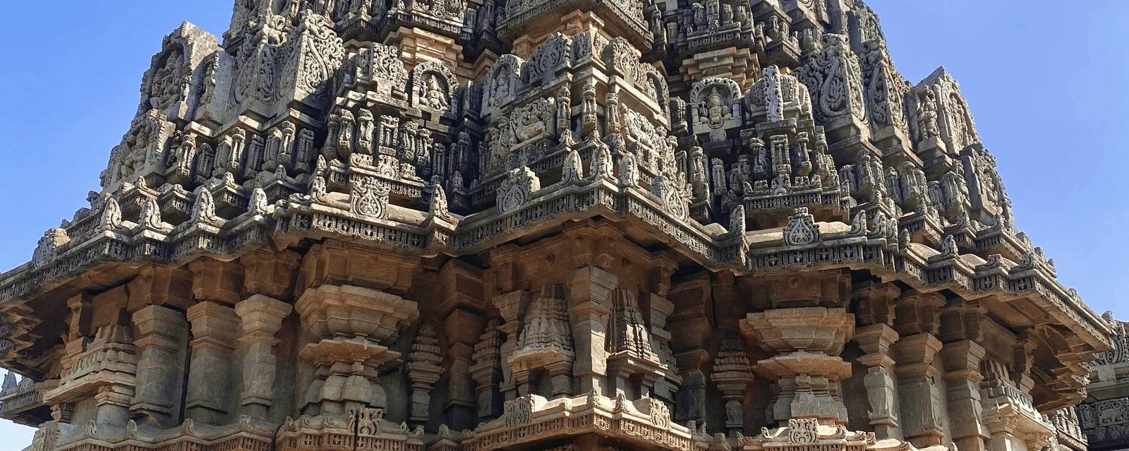 A close-up of an ornate historic Indian temple spire with intricate stone carvings under a clear blue sky.