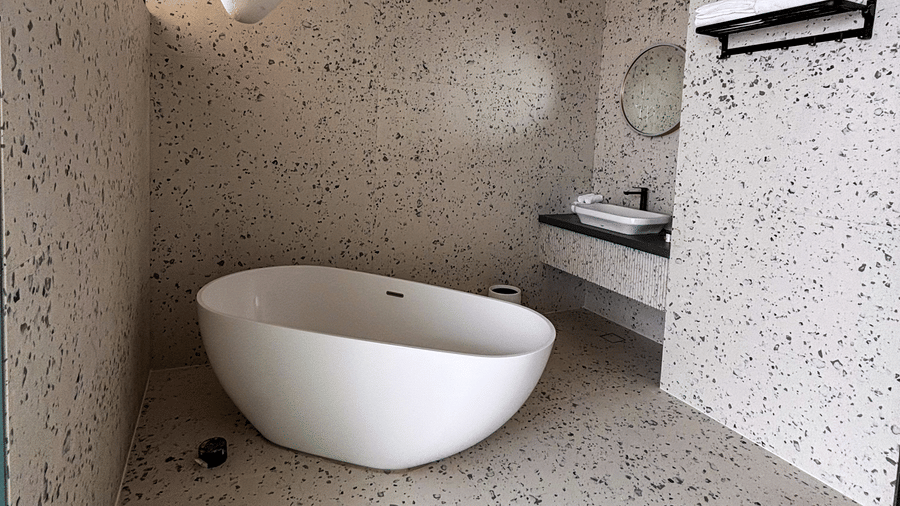 A white oval bathtub stands on a terrazzo floor in a bathroom with matching speckled walls and a vanity at Avanya Resorts N Retreat.