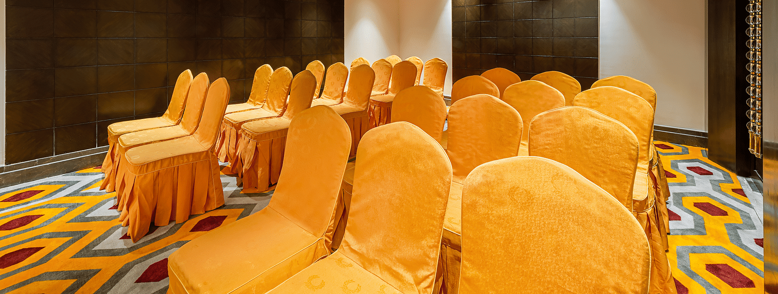 Conference room with yellow-orange chair covers, a dark tiled wall and a patterned carpet - TGI Grand Fortuna, Hosur