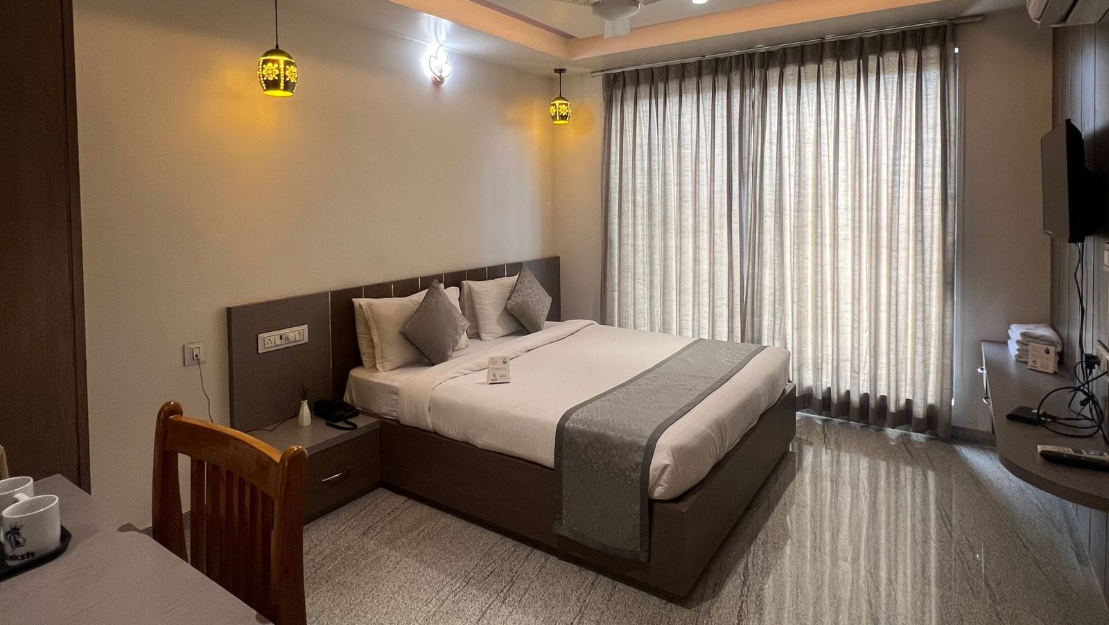 Wide view of the Daksh Comfort Room at Daksh The Valley Resort, Saputara, showcasing its centrally placed king size bed, closed curtains, warm overhead lighting, and marble flooring.