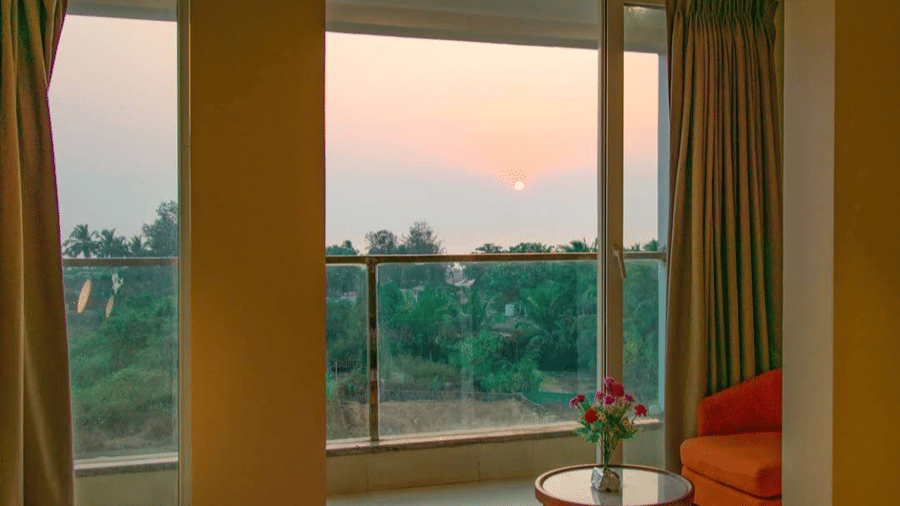 A view from a room through glass doors with an orange chair on a balcony at sunset at Estherea Elite, Morjim.