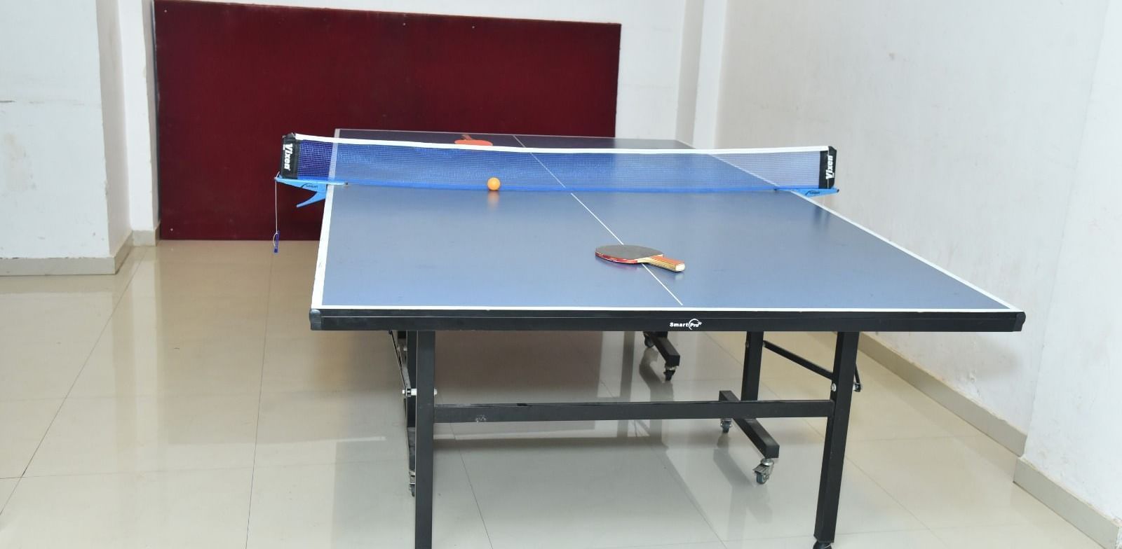A table tennis setup in an indoor room with a table, net, two paddles, and a ball placed on it, at Highland Resort.