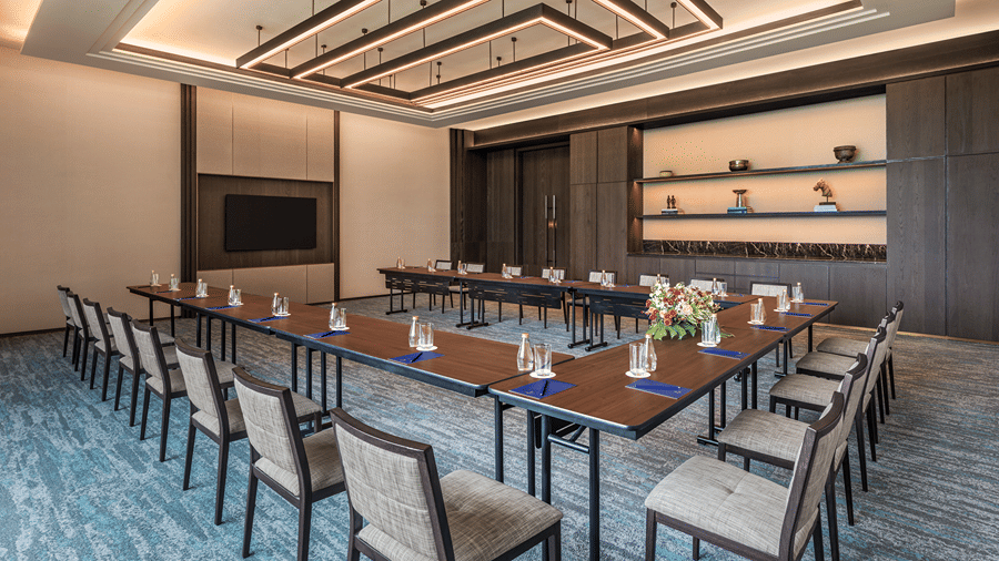 Council 2 meeting room in a U-shape layout with notepads, water bottles, a floral centrepiece and a wall-mounted screen at The Residency Signature Madurai.