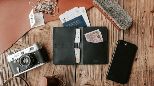 A black leather wallet, a camera, earphones and passport placeed on a wooden table.