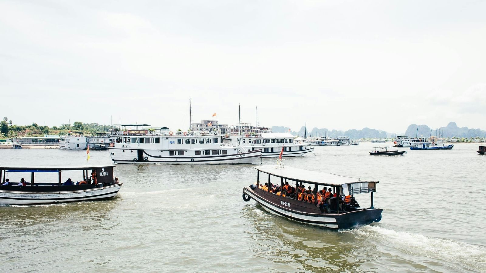 Several boats docked in waters with distant buildings under a clear sky.
