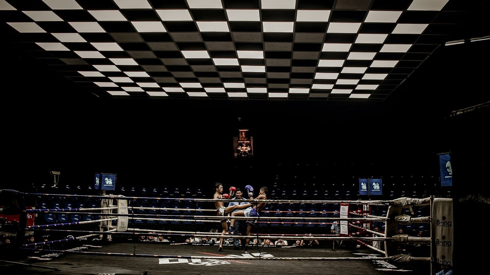 two muay thai fighters fighting inside a ring with a referee behind them officiating