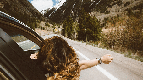 A girl siting in a car with her hand wide open feeling the gentle breeze.