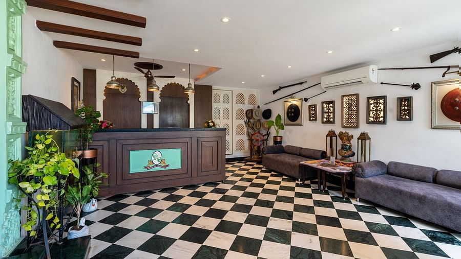 Reception area at Panna Vilas Palace features a wooden reception desk, walls adorned with wall-mounted frames, and several potted plants | Panna Vilas Udaipur