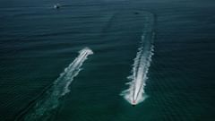Two jet skis racing across the open sea, leaving long white trails on the deep blue water.