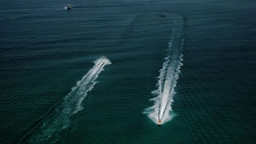 Two jet skis racing across the open sea, leaving long white trails on the deep blue water.