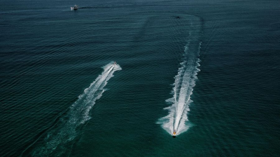 Two jet skis racing across the open sea, leaving long white trails on the deep blue water.
