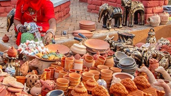 A person arranges handcrafted clay pots and decorative items on a tiered display for sale.