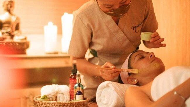 A therapist performing a massage in a warmly lit spa room with candles and flowers at Karma Chalets.