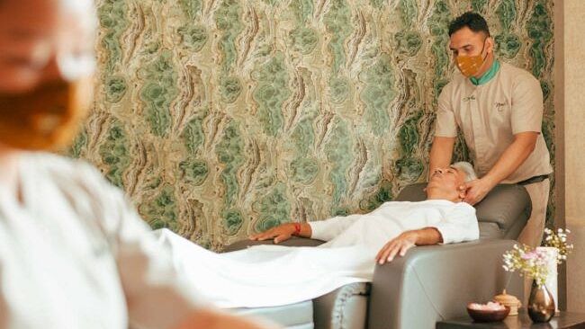 A person receiving a massage in a spa room with patterned green wallpaper and a therapist in the background at Karma Chalets.