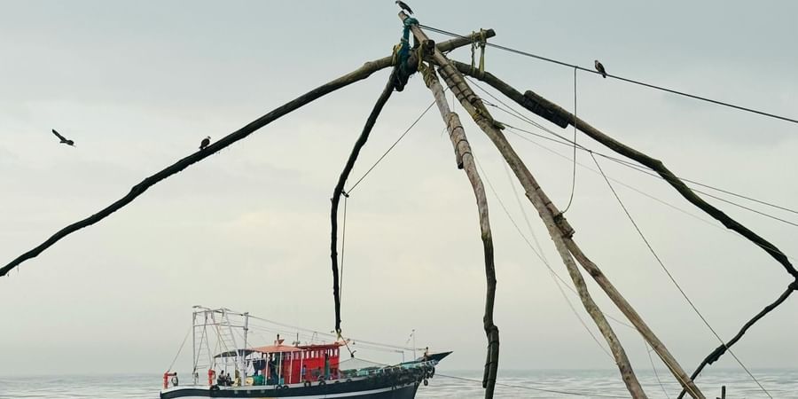 A Chinese fishing net structure by the waterfront, with a boat in the background.