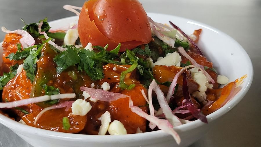 Fresh salad bowl with tomatoes, onions, and greens on a stainless steel counter at Dagshai Manor Kasauli - Inde Hotels.