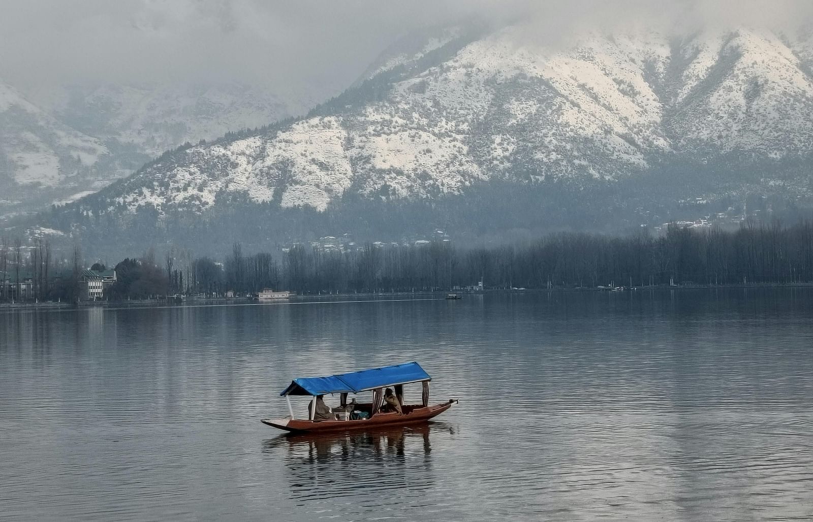 A picture of a serene lake with a single boat and snow-capped mountains in the background.