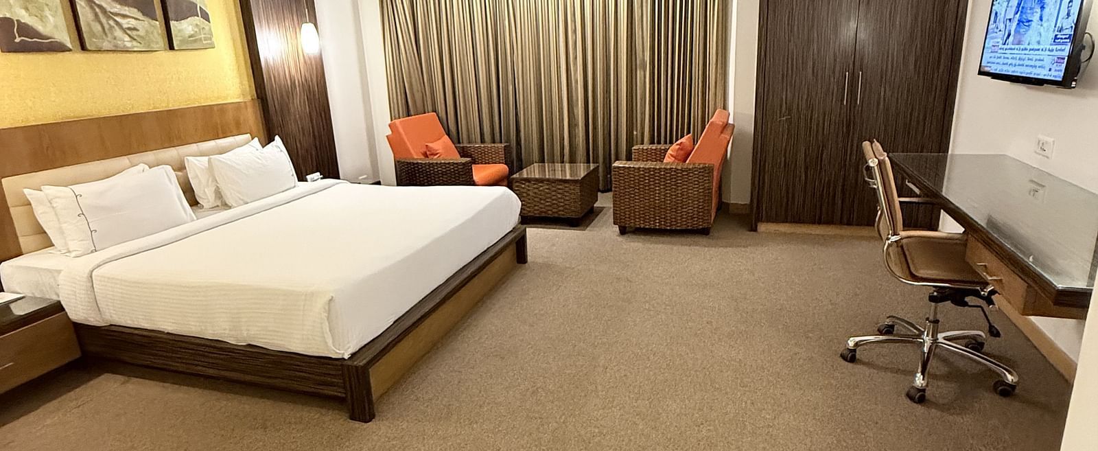 A spacious room with a large bed, cushioned seating beside the window with curtains, and a TV with a writing desk to the side | Cenneys Gateway