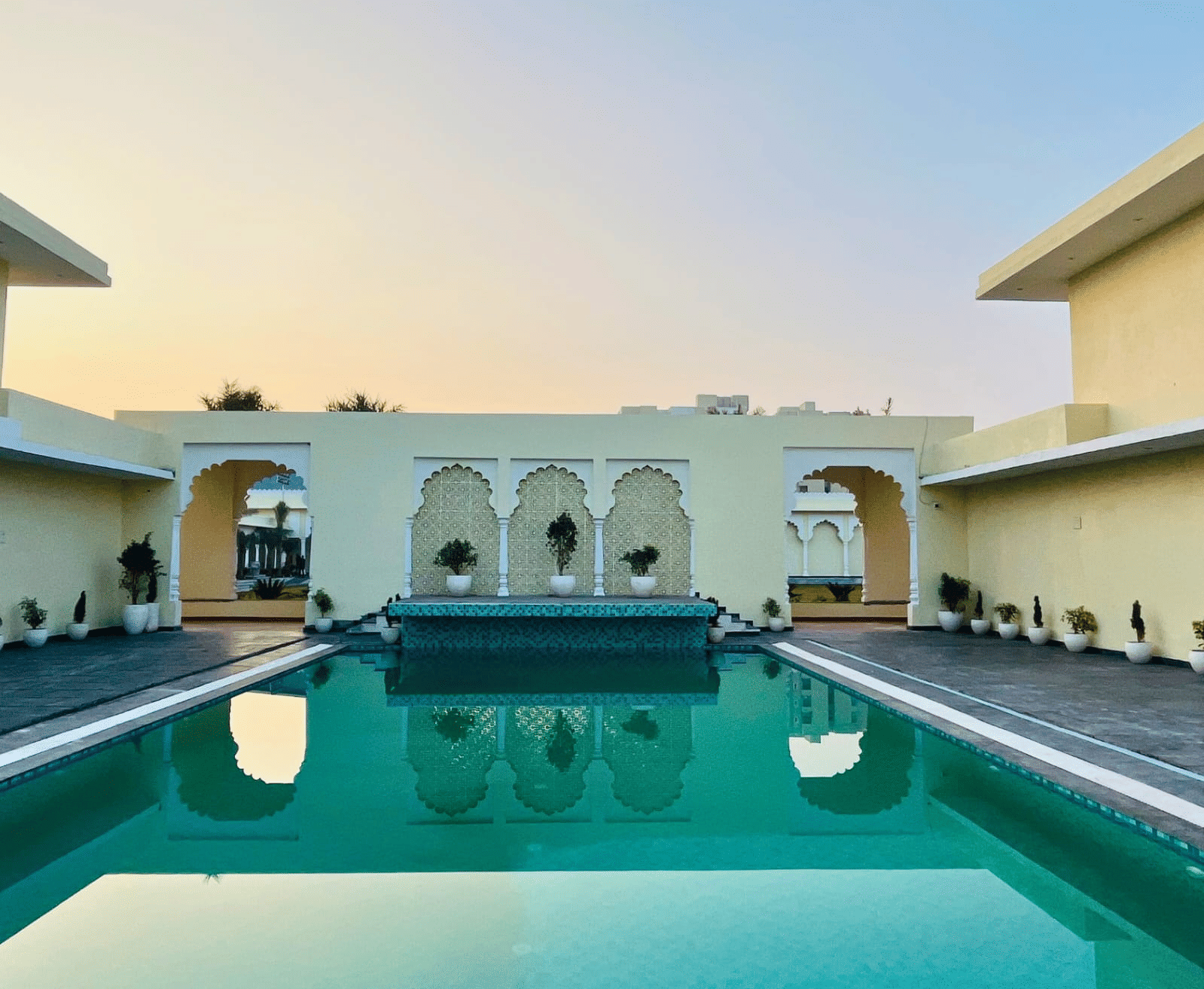 Outdoor swimming pool surrounded by arched buildings with seating areas at Beelwa Palace, Jaipur