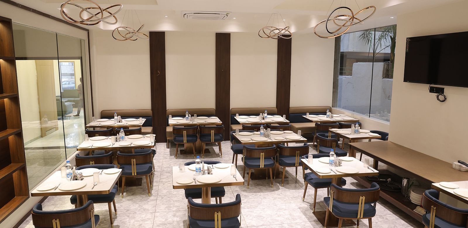 A brightly lit dining area at Lords Eco inn Jamnagar Maheshwari Nagar with multiple tables chairs and stylish lighting.
