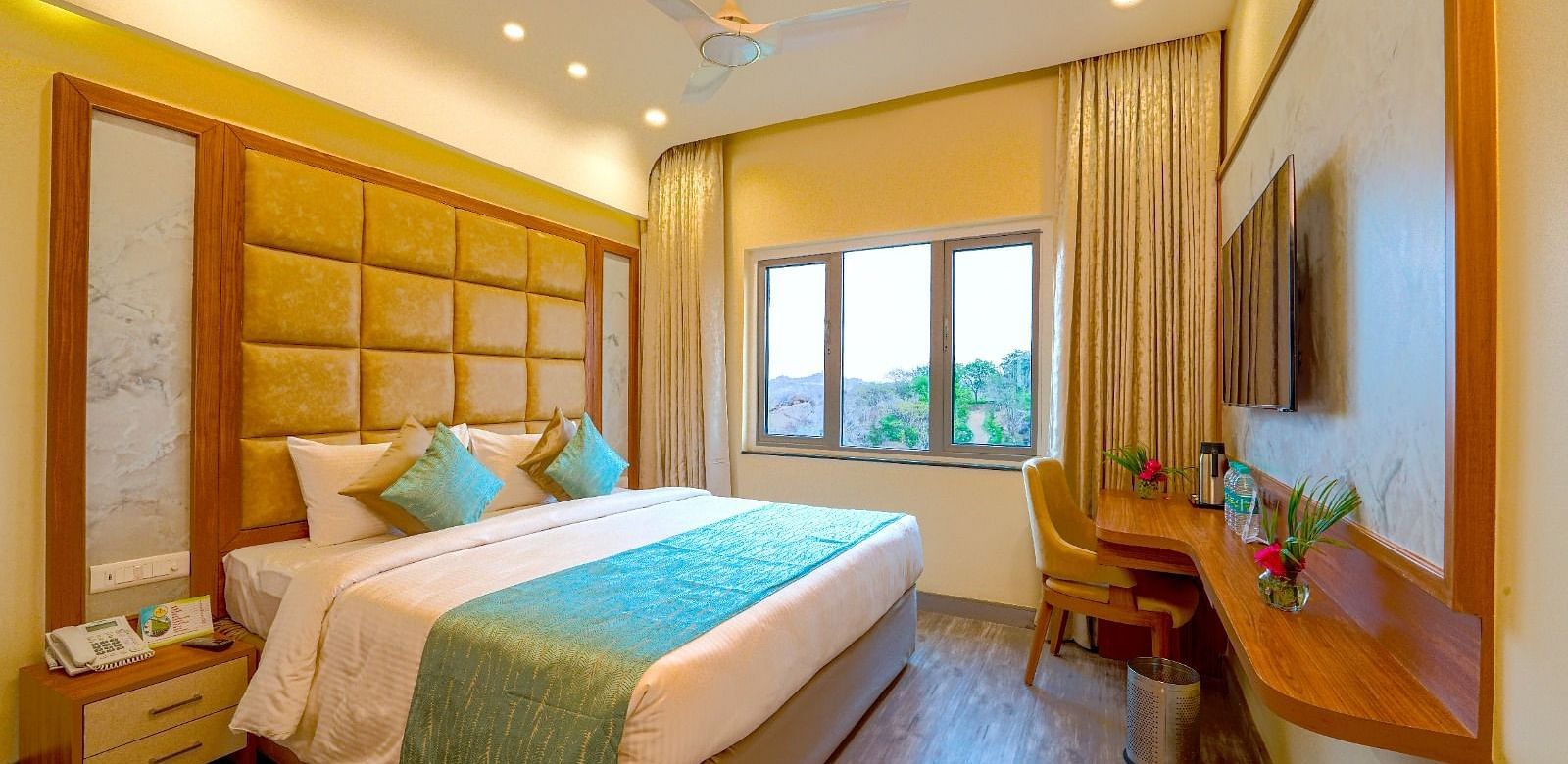 Cozy bedroom with a queen-sized bed, elegant headboard, and large window offering natural light at Tara, Comfort Hotel in Hyderabad - Ramoji Film City.