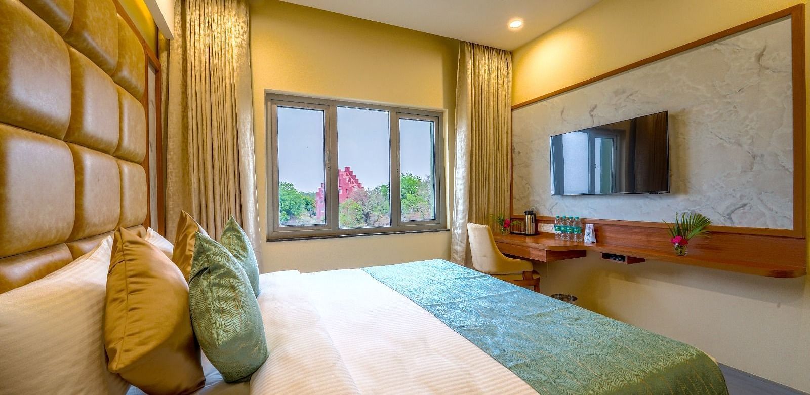 Bright and airy hotel room with a plush queen-sized bed, wooden accents, and a view of the greenery outside Tara, Comfort Hotel in Hyderabad - Ramoji Film City.