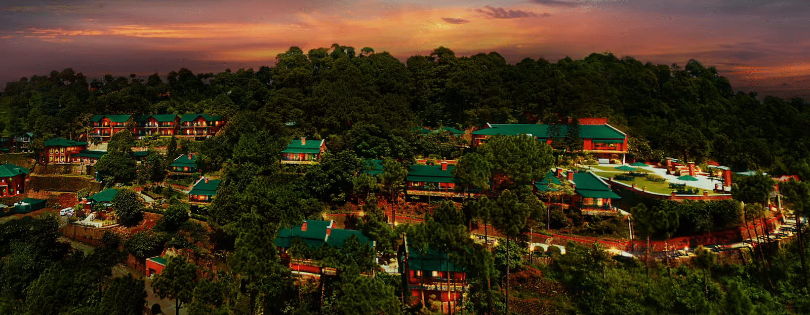 An aerial view of villas perched atop a mountain in the evening, with the sun setting behind them, casting a warm glow