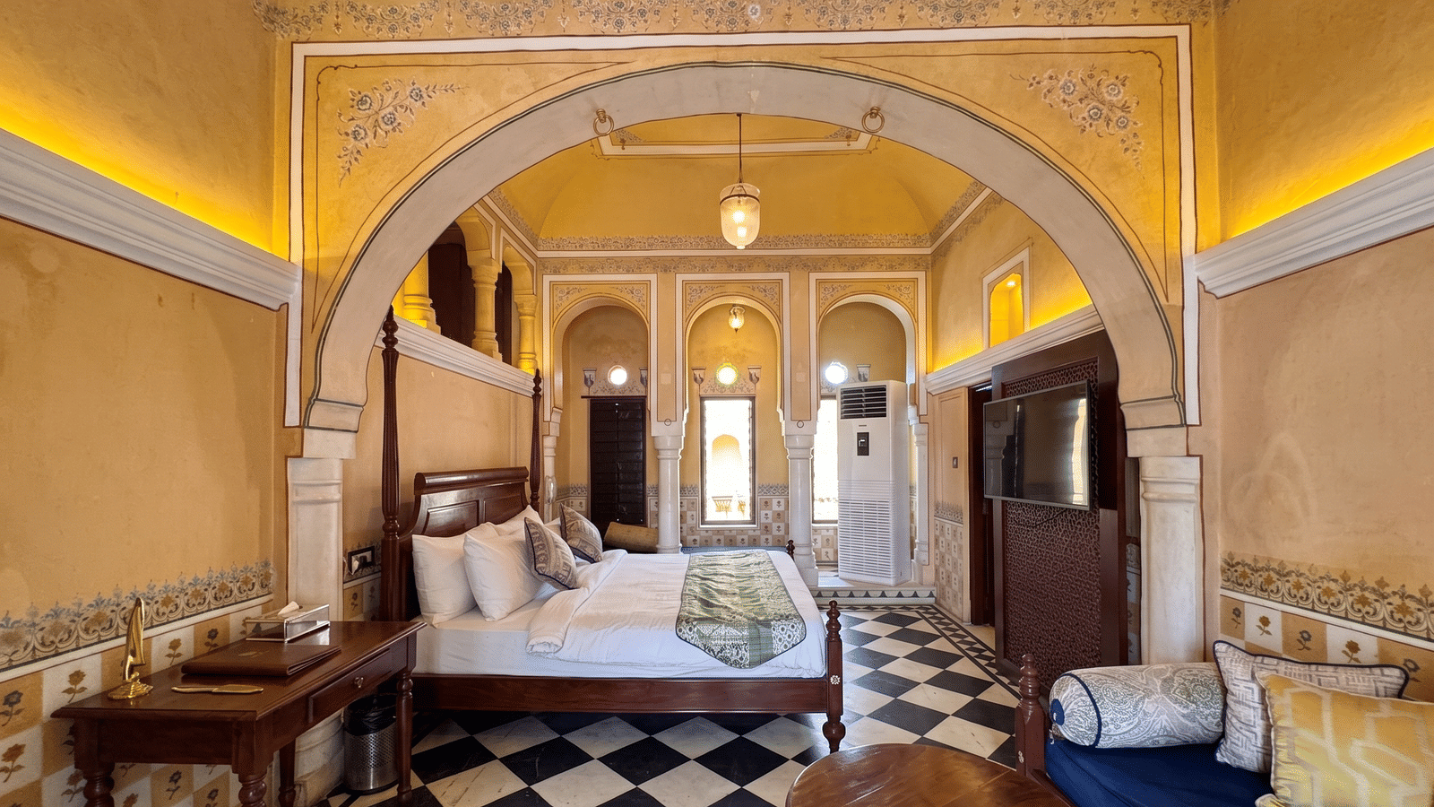 Heritage bedroom with a four-poster bed, painted archway, chequered marble floor, daybed seating and wall-mounted TV at BluSalzz Vintage - Harlalka Haveli.