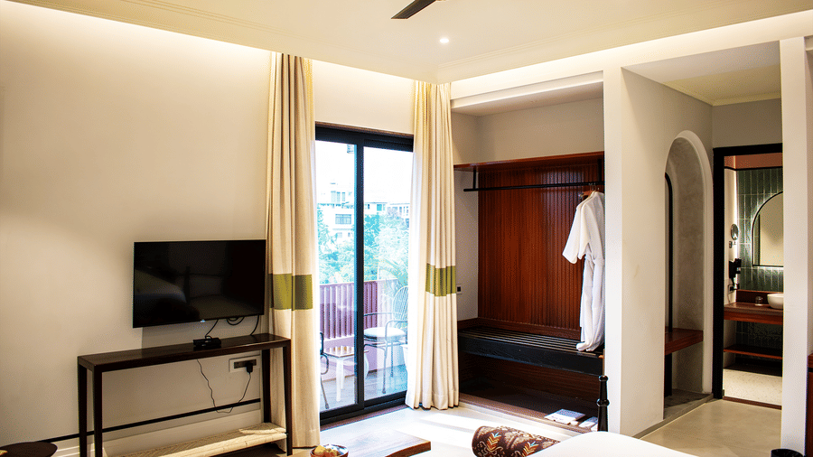 A bedroom at The Sierra - By The Lake featuring a television on a wooden console table, a glass balcony door with curtains, and an open wardrobe area.
