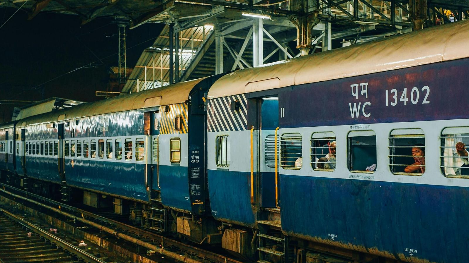 Side view of a blue and white Indian passenger train stopped at a platform.