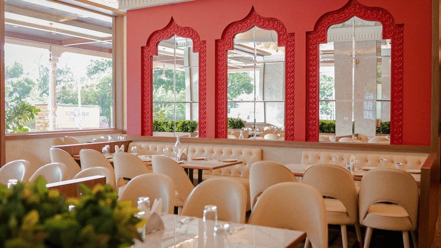 Tables and chairs in a restaurant area with a bright red feature wall containing arched mirrors at Hotel Mumbai House Digha, Airoli.